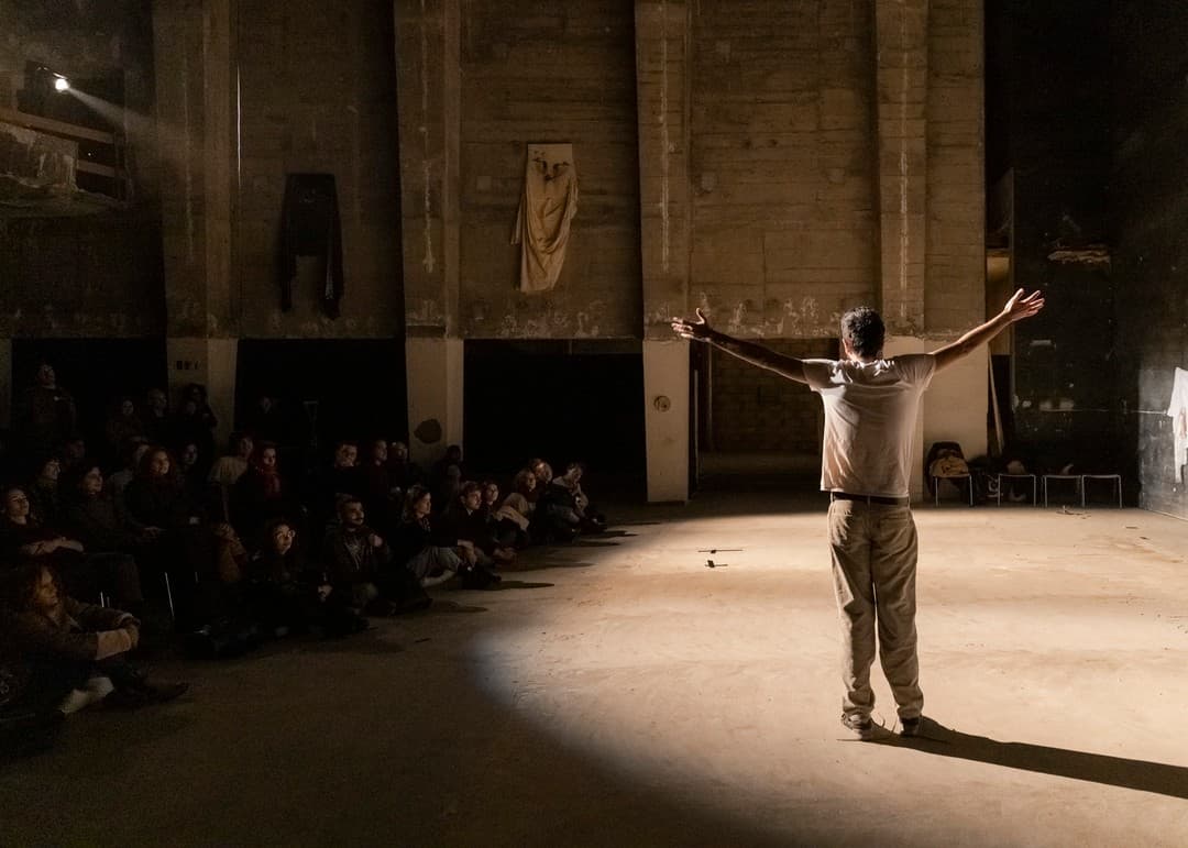 Fadi Murad, arms outstretched in a pool of light, performing to a seated audience at Les Urbaines in Lausanne.